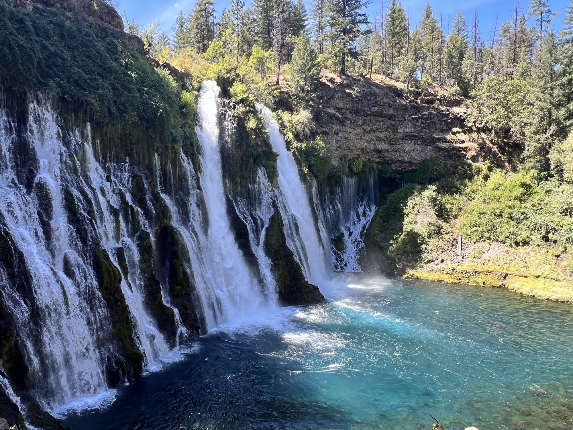 Many streams of a waterfall pouring into a turquoise pool